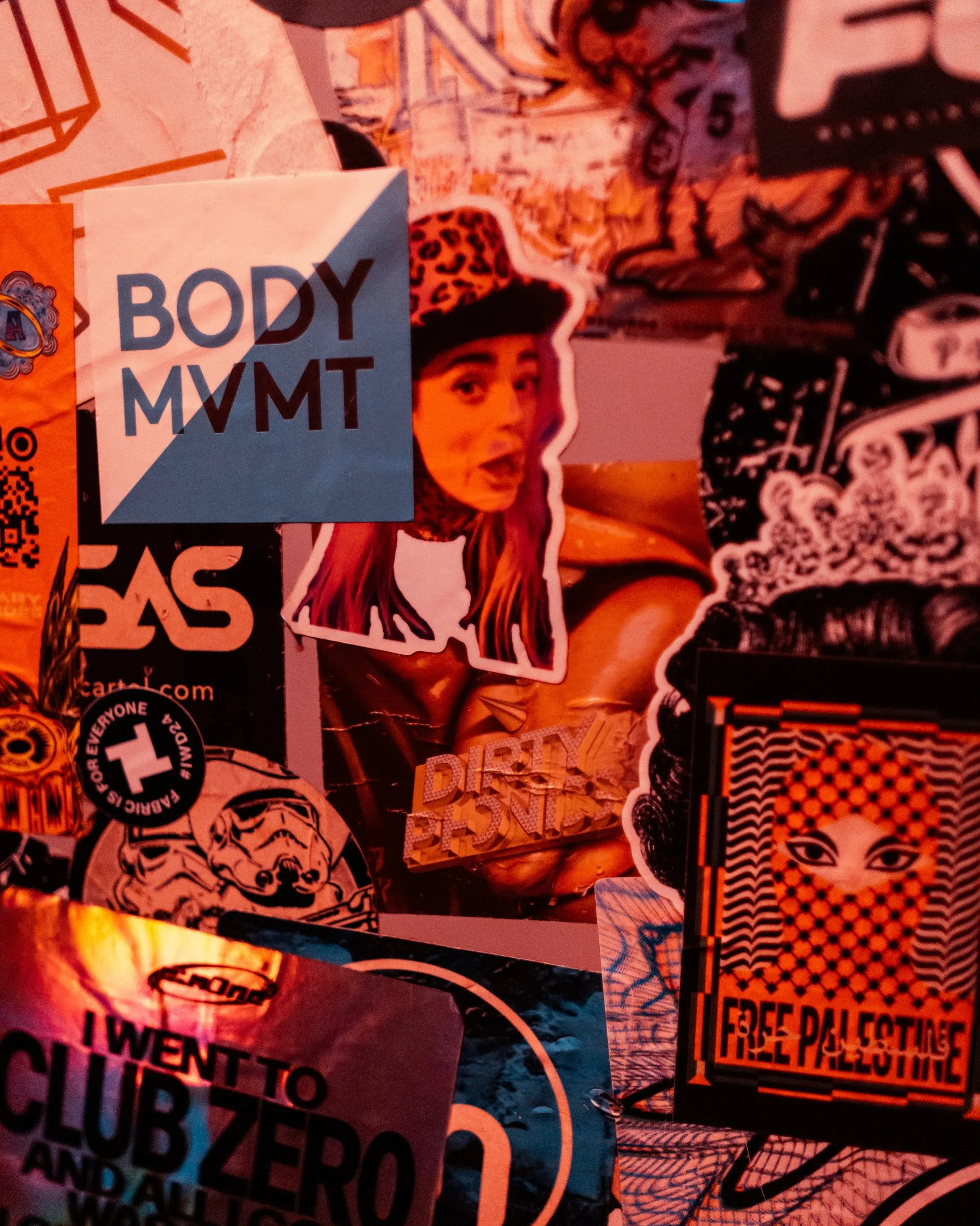 Collage of various stickers, including a prominent one with a woman's face and text that reads 'BODY MVMNT', a sticker with the word 'DITTY', and others with different patterns and symbols in black, white, orange, and blue colors.