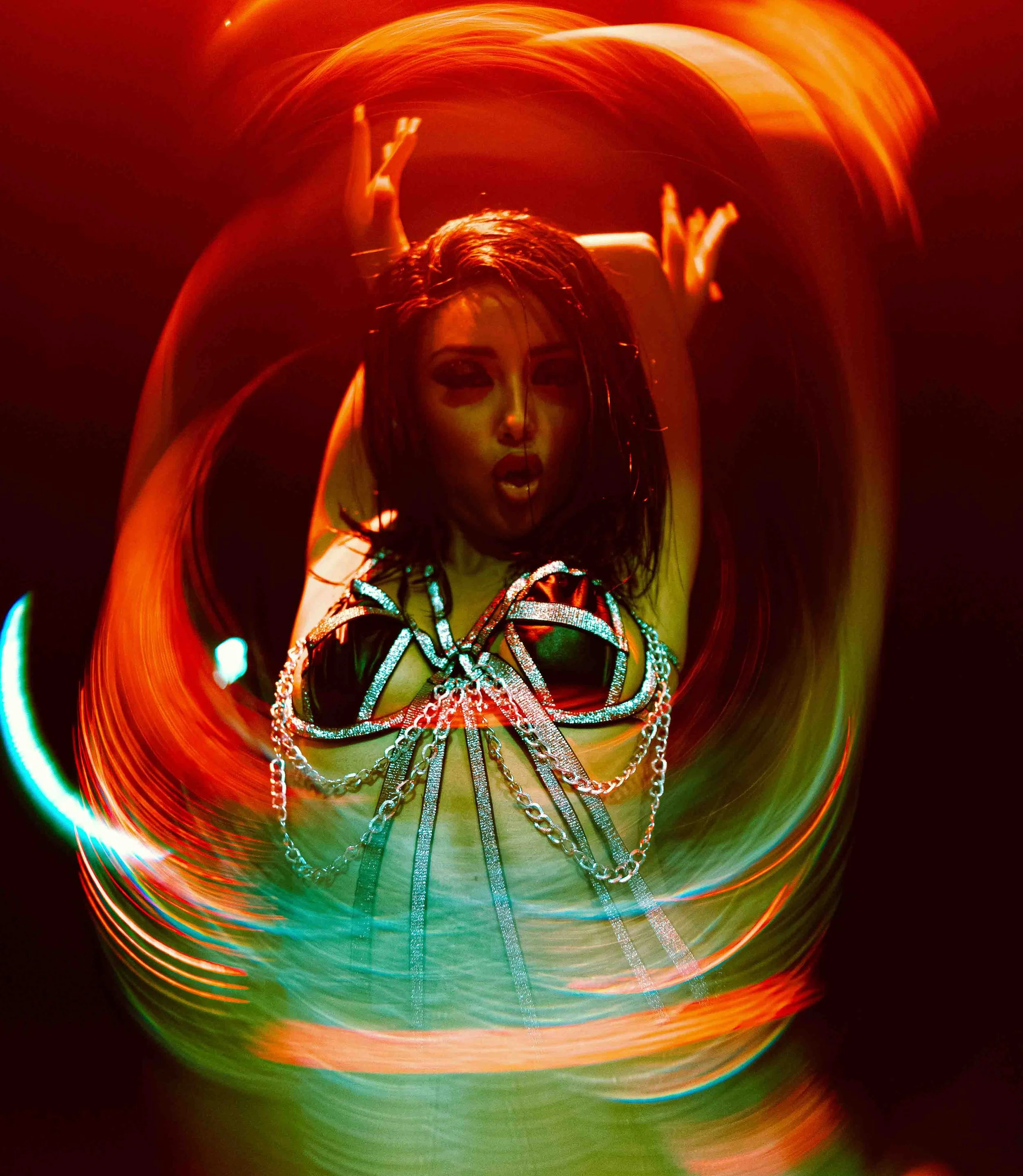 A woman dances amidst colorful, swirling light trails in a dark setting, creating a vibrant, abstract visual effect.
