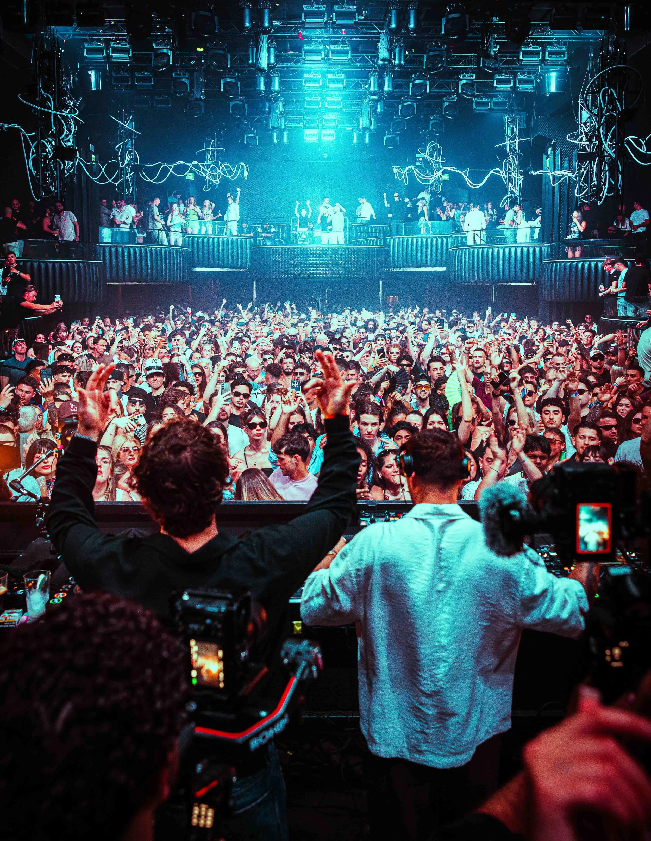 Crowd of people dancing and enjoying music at a nightclub with DJ playing on stage.