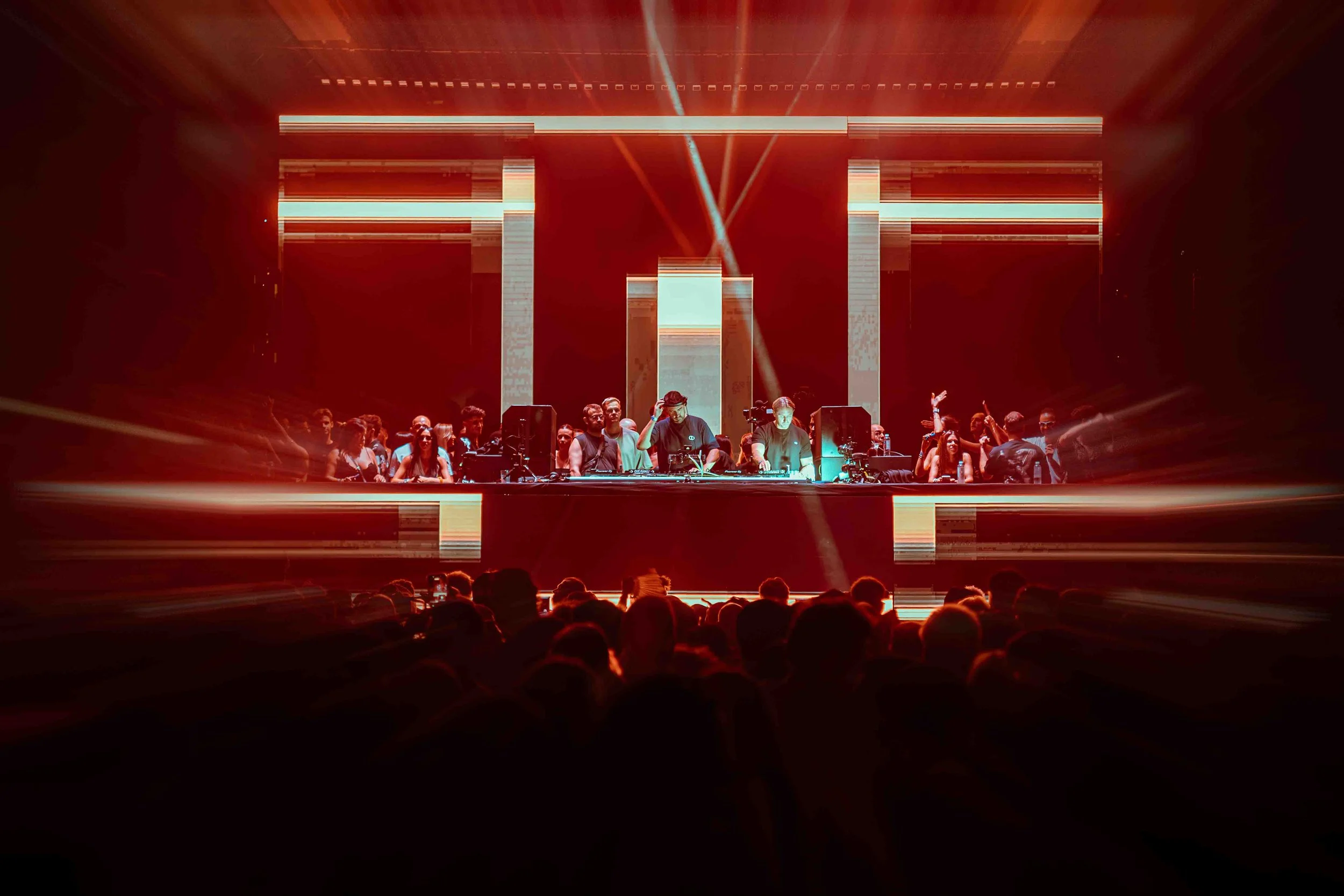 A lively nightclub scene featuring a DJ on stage with people dancing and enjoying the music, illuminated by colorful lights and a vibrant atmosphere.