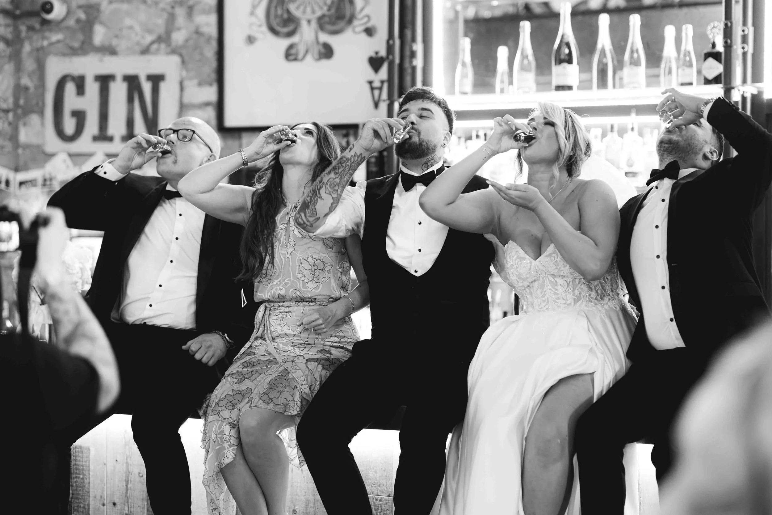 People sitting at a table, drinking shots, at a celebration or party, with a bar in the background.