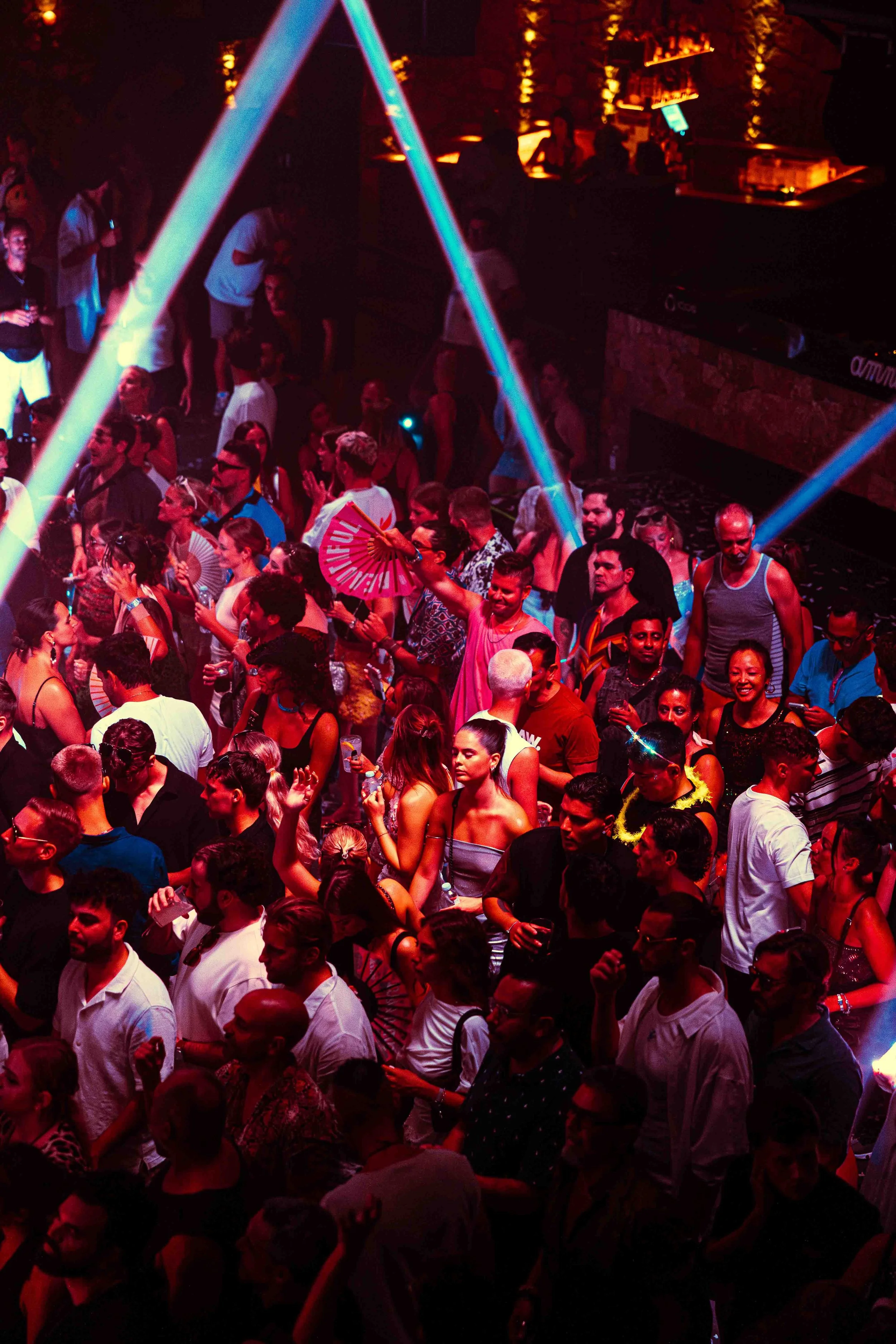 Crowd of people at a nightclub with neon lights and colorful decorations.