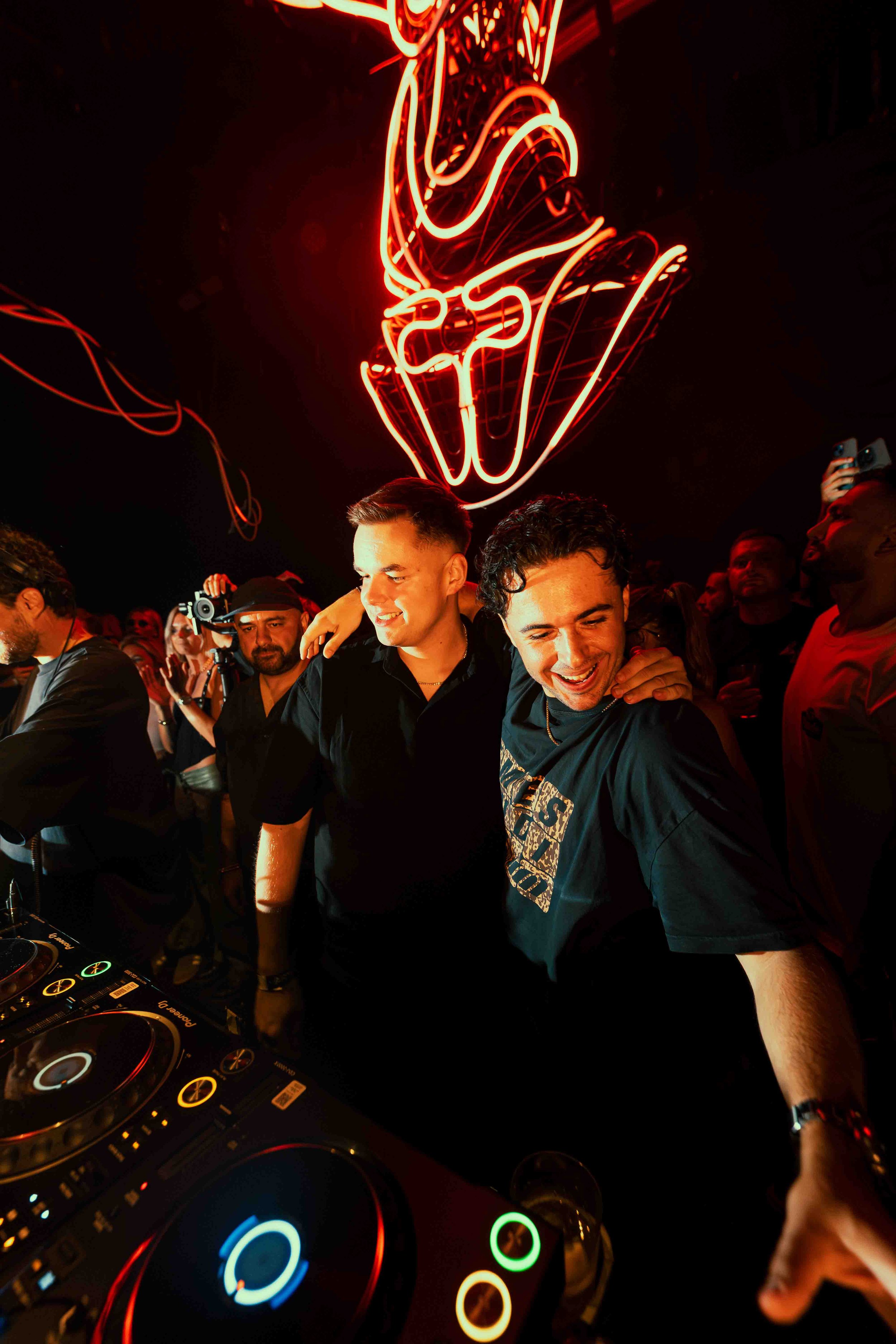 People dancing and enjoying themselves at a nightclub, illuminated by a large neon red ice cream cone sign hanging from the ceiling.