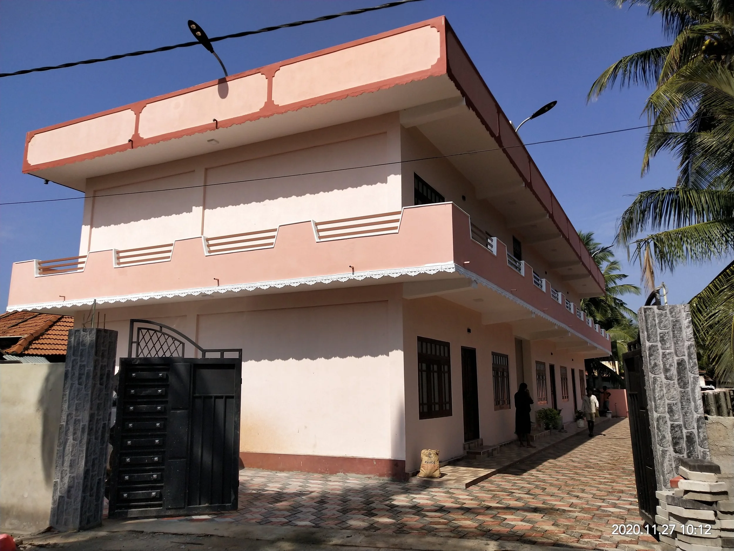 A pink and white three-story building with balconies, surrounded by palm trees under a clear blue sky.