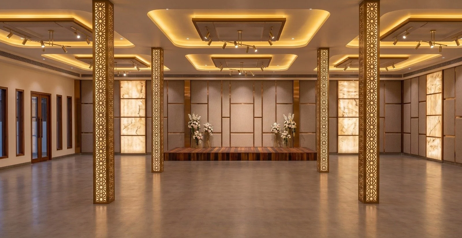 Elegant, spacious banquet hall or event space with warm lighting, wooden accents, and flower arrangements on a stage.