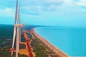 View of a coastline with wind turbines near the ocean under a partly cloudy sky.