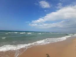 Sunny beach with waves crashing onto the sandy shore and a partly cloudy sky.