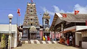 Thiruketheswaran Hindu temple with multiple towers and flags, surrounded by smaller buildings and statues, under a blue sky.