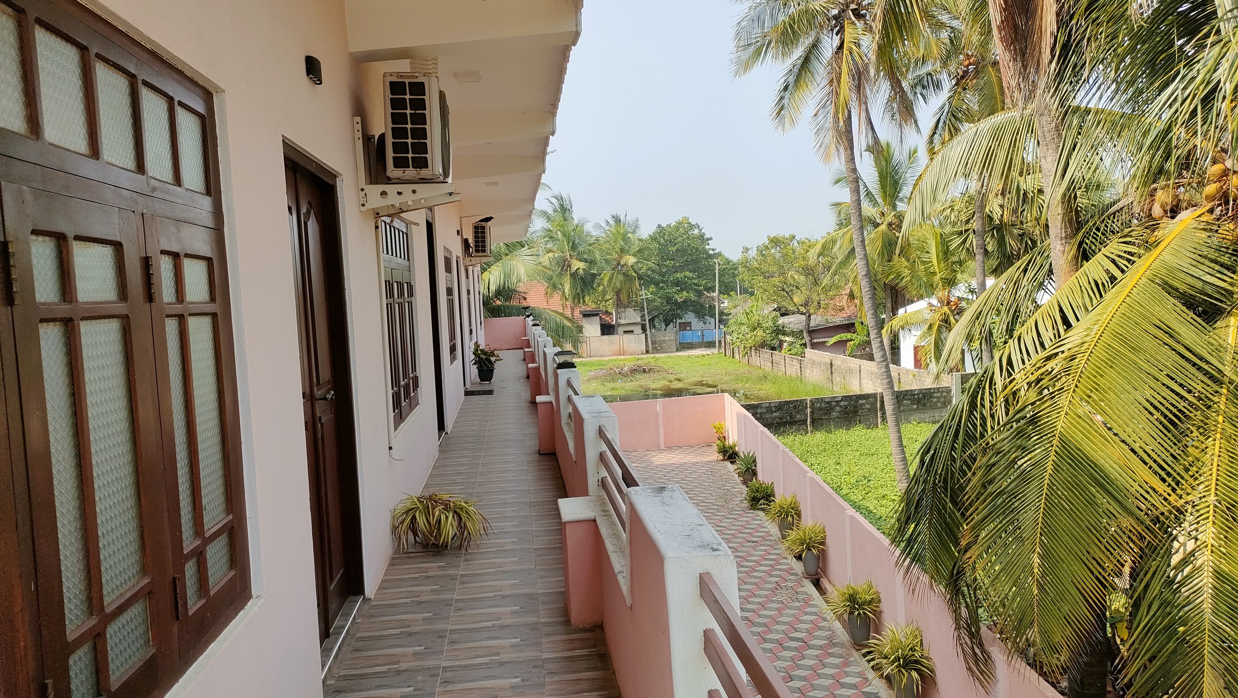 Balcony with potted plants, wooden door, and views of trees and neighboring houses.
