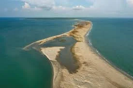 A sandbar extending into the ocean with calm water surrounding it.
