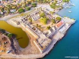 Aerial view of a historic coastal fortress with thick walls, surrounded by water on multiple sides, featuring a park and a small harbor with boats nearby.
