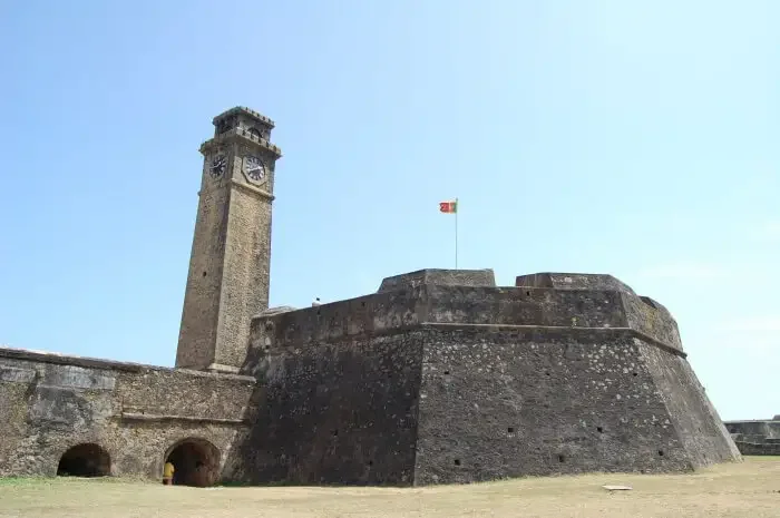 Historic Mannar stone fort with a tall clock tower and a small flag flying on top, against a clear blue sky.