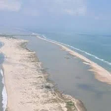 View of a beach with a narrow sand barrier and shallow water channels, extending into the ocean.