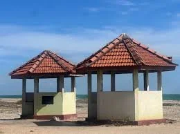 Two small beach huts with red tiled roofs by the sea under a blue sky