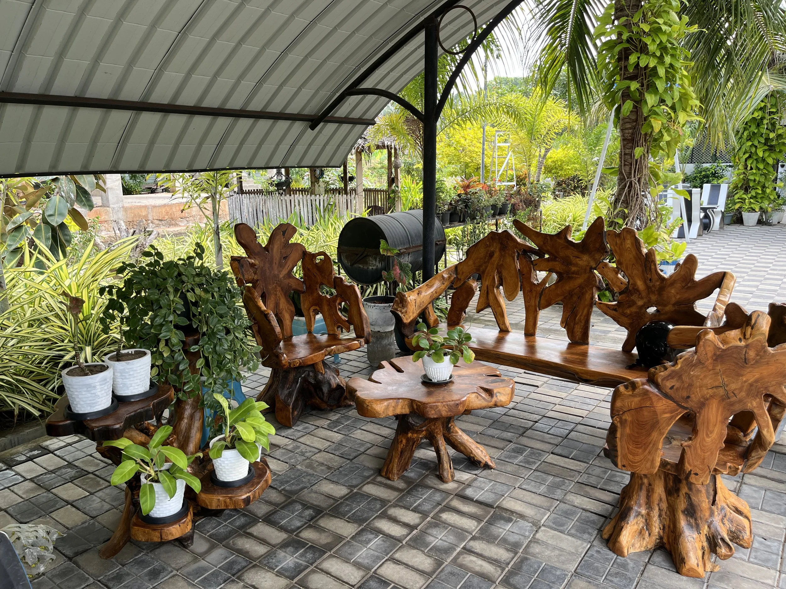 Outdoor patio area with wooden furniture, potted plants, trees, and a metal roof canopy.