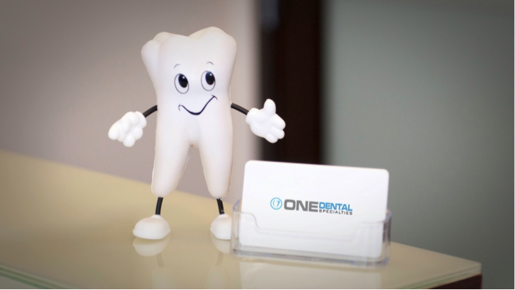 A cartoon character of a tooth with eyes, a mouth, and arms giving a thumbs up next to a dental office sign.