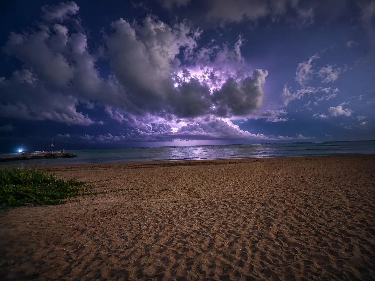 A beach at night with dark clouds and lightning in the sky.