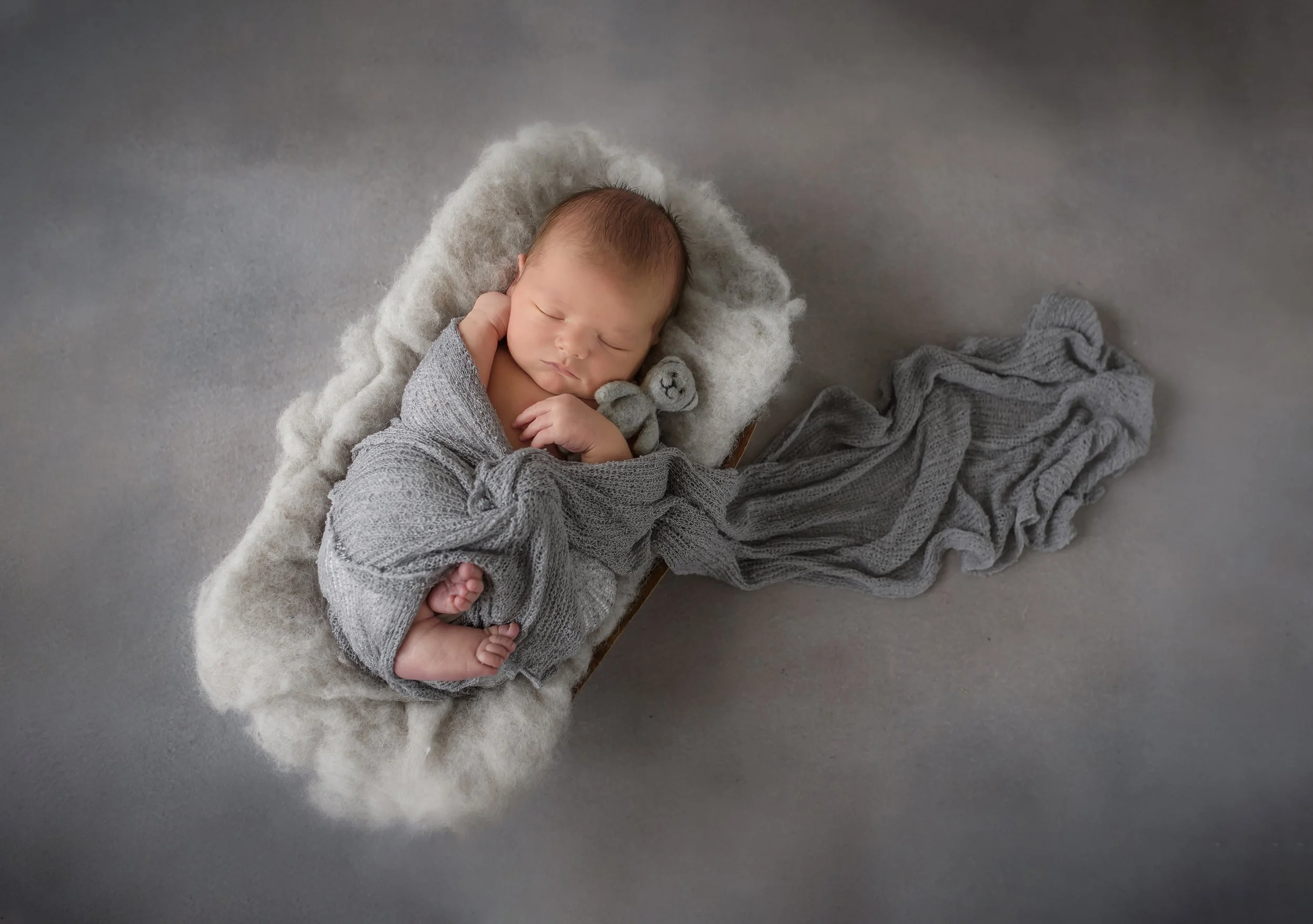 A sleeping newborn baby laying on a soft, fluffy blanket while holding a small teddy bear.