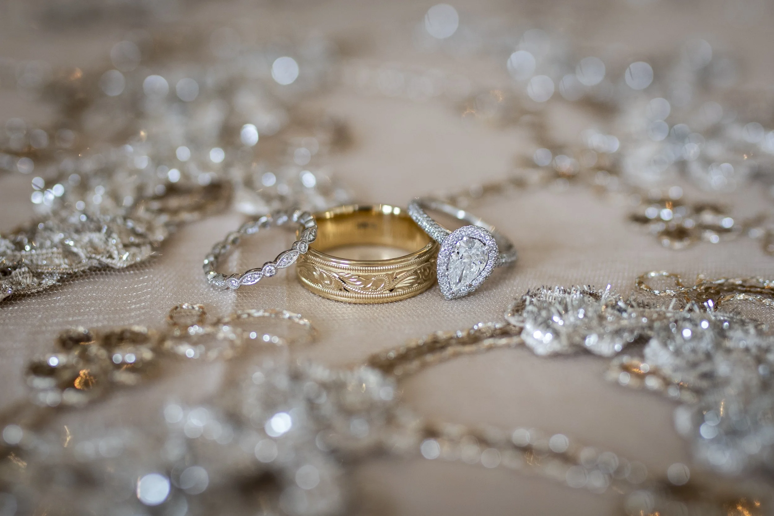 Close-up of sparkling jewelry and rings on a beige fabric surface, with a blurred background of shiny, reflective jewelry pieces.