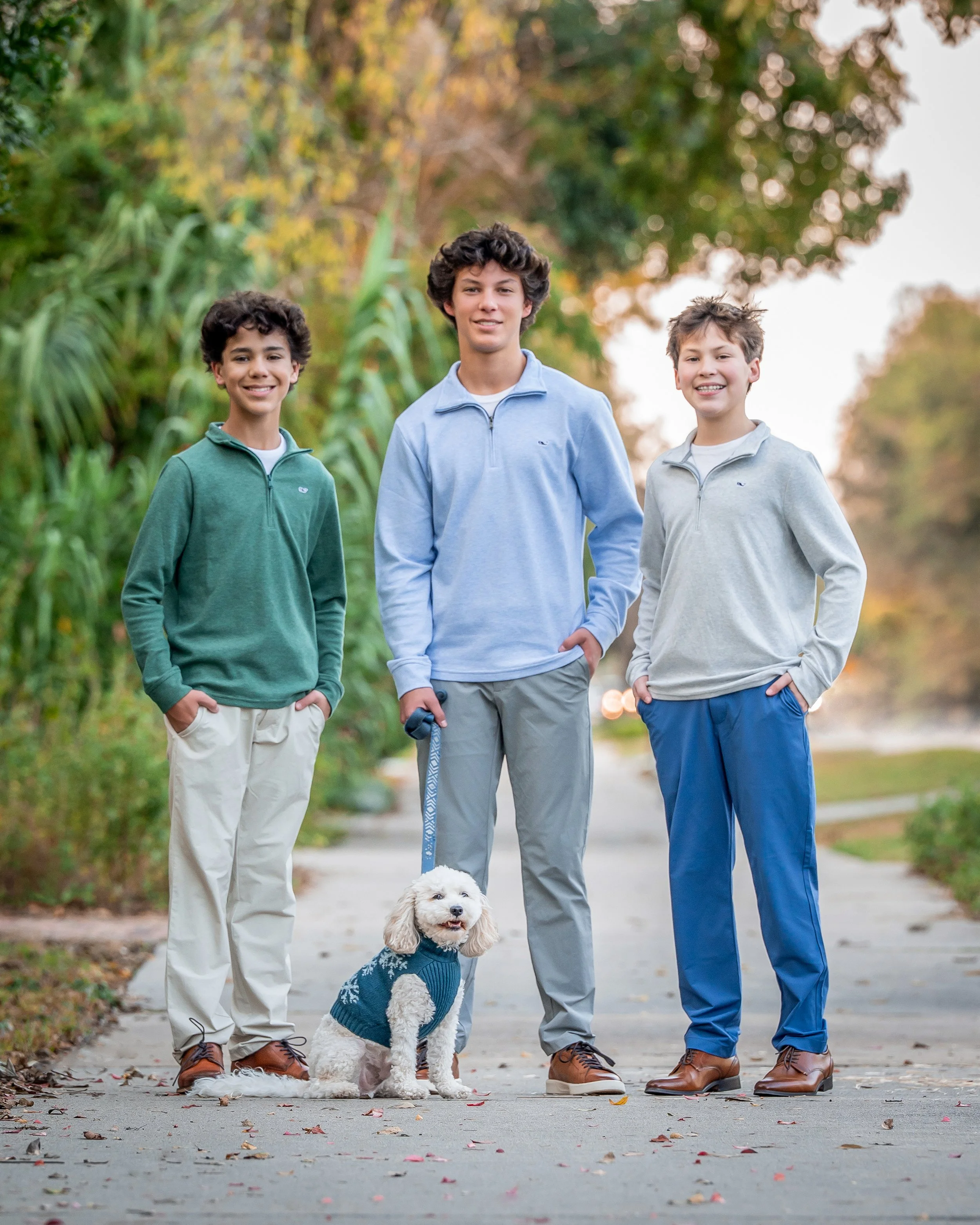Three boys with a dog walking on a park trail during fall.