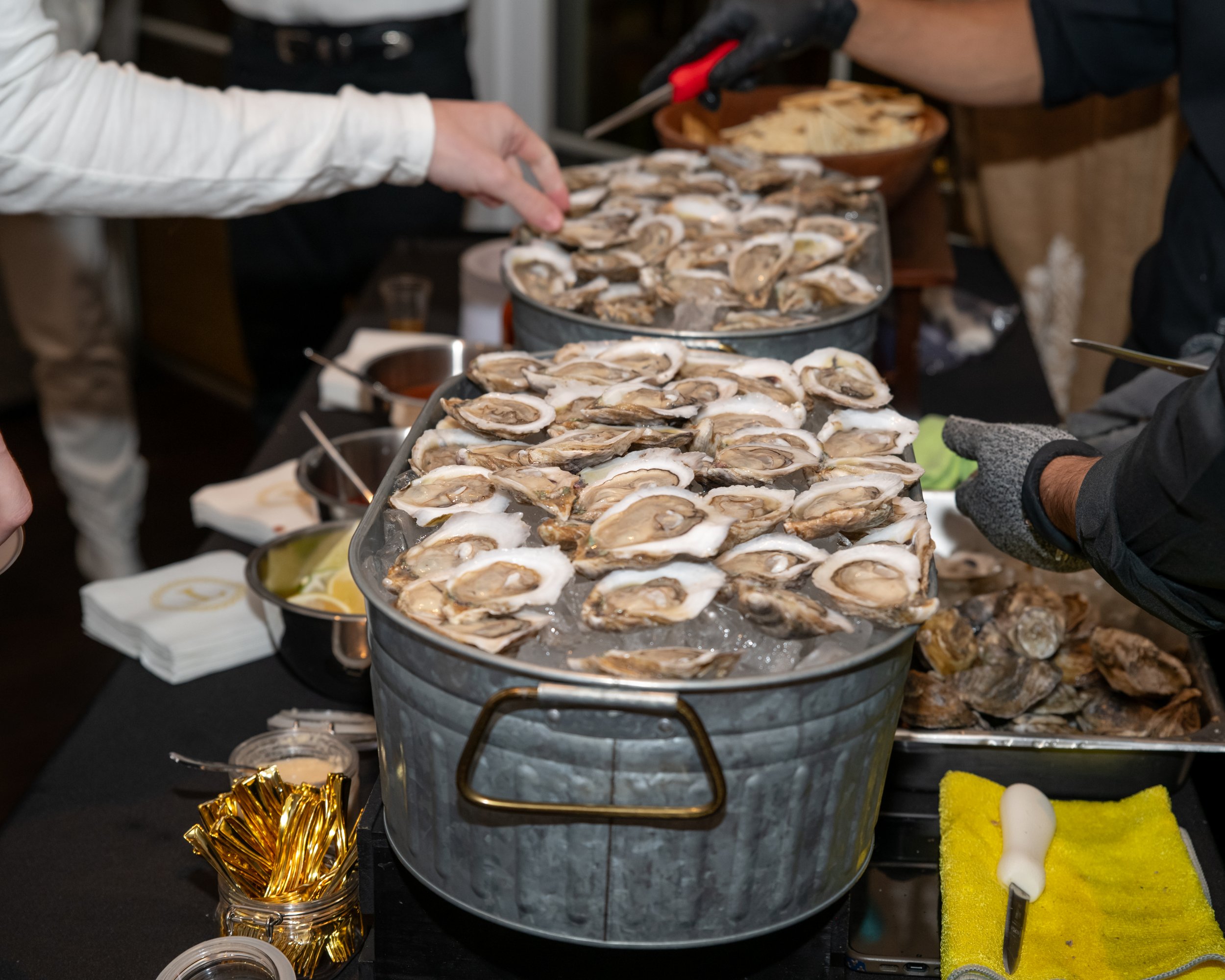 A buffet table with trays of oysters on ice, a bowl of chips, and party decorations.