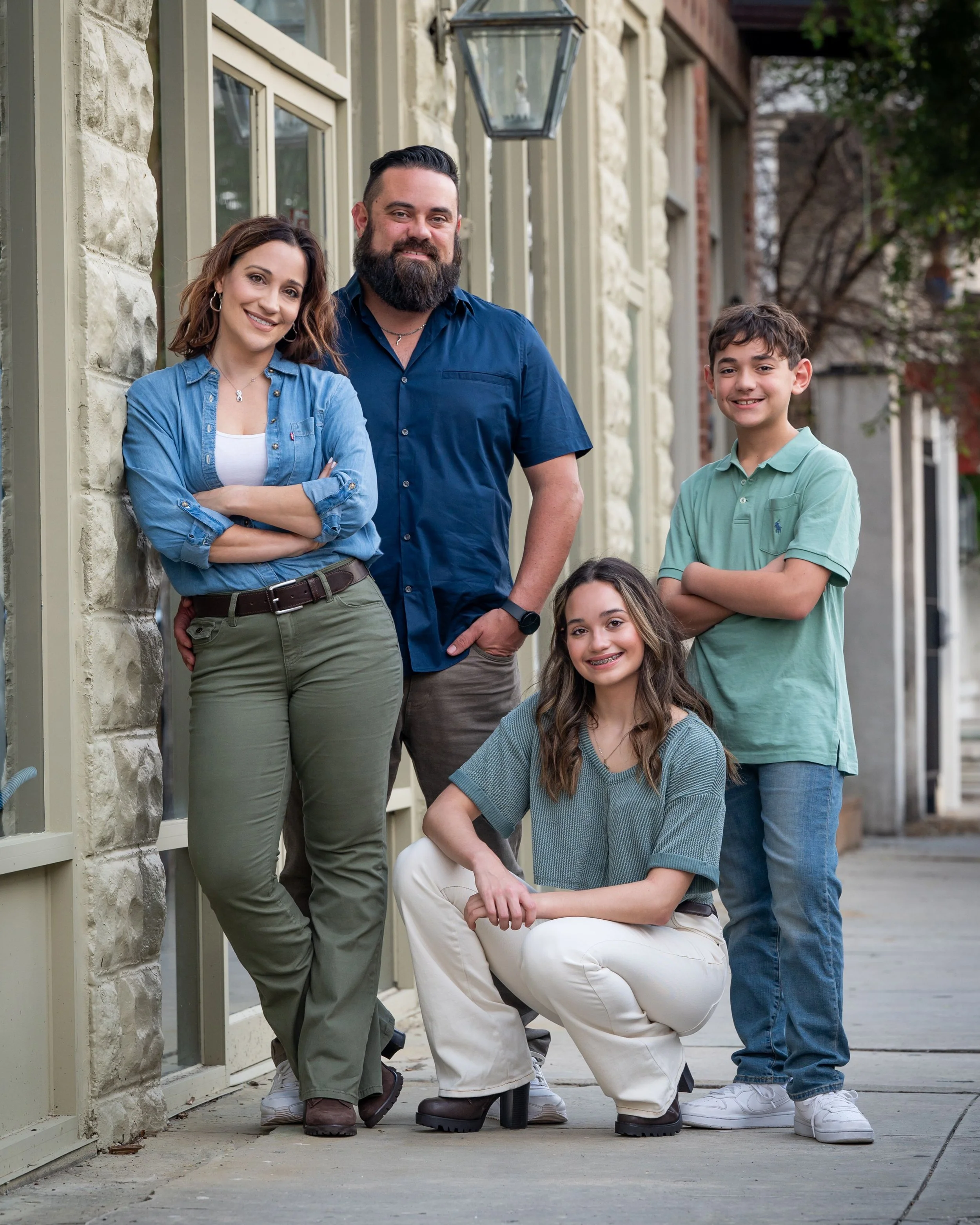 Family standing and sitting outside near a stone building with large windows and an outdoor lantern. They are smiling and posing casually.