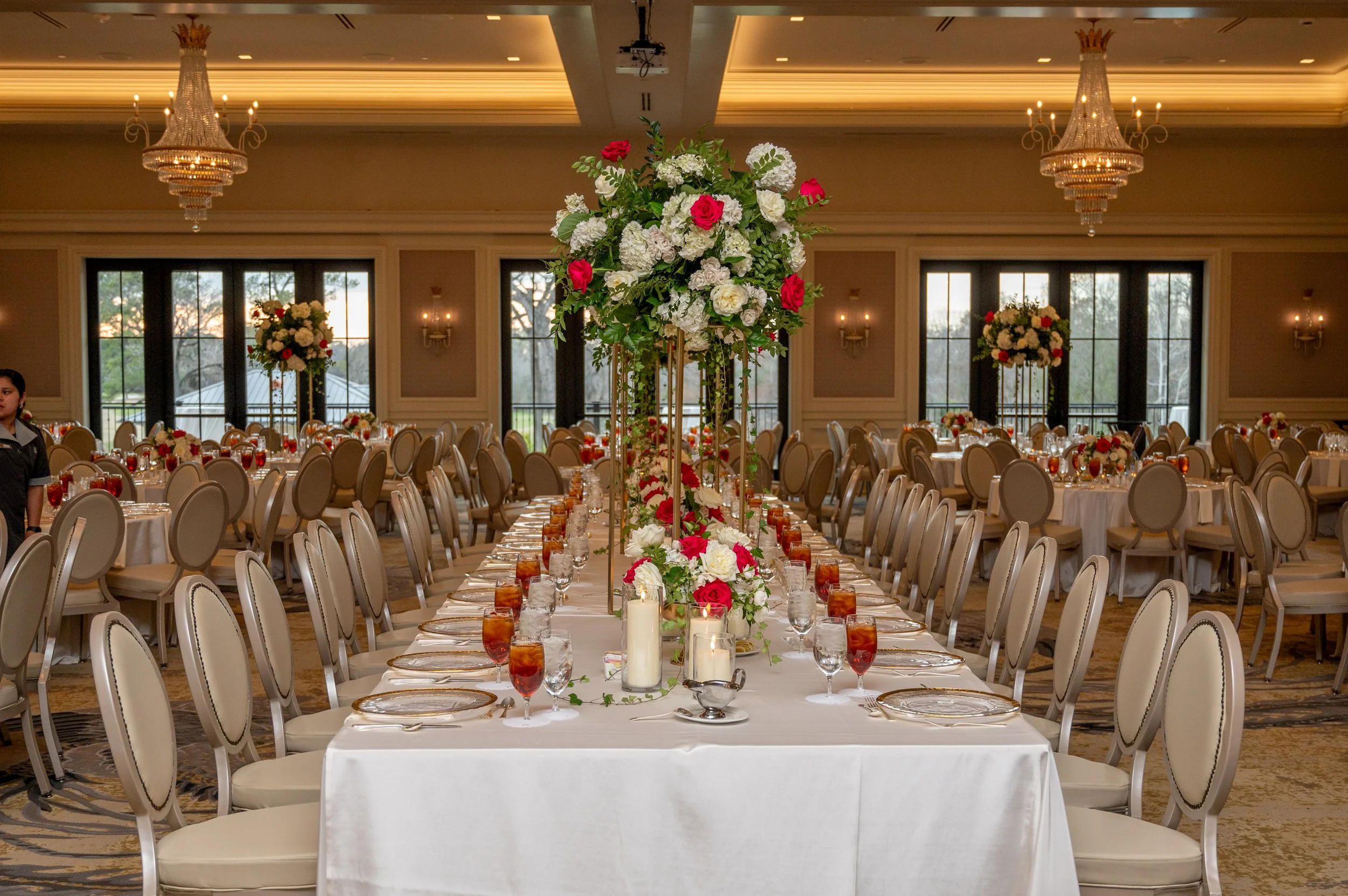 Elegant banquet hall decorated for a wedding or special event with round tables, white tablecloths, floral centerpieces, candles, and chandeliers.