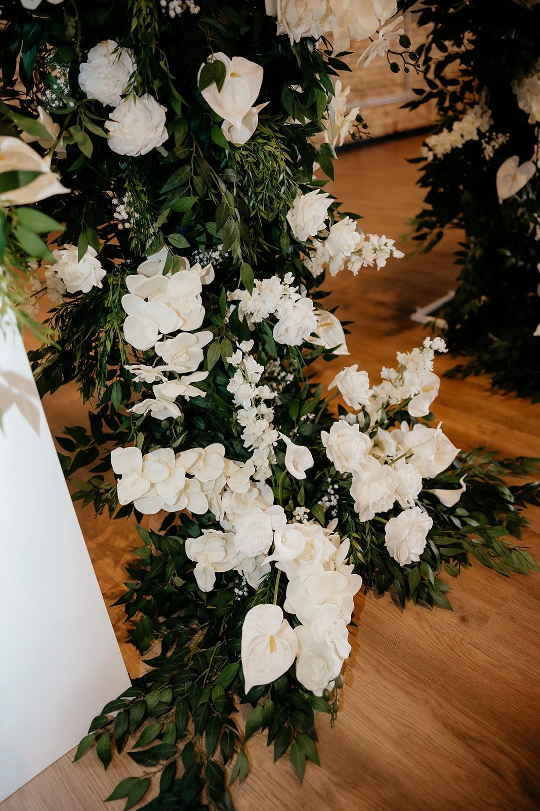 White floral decoration with flowers and green leaves on a wooden floor.