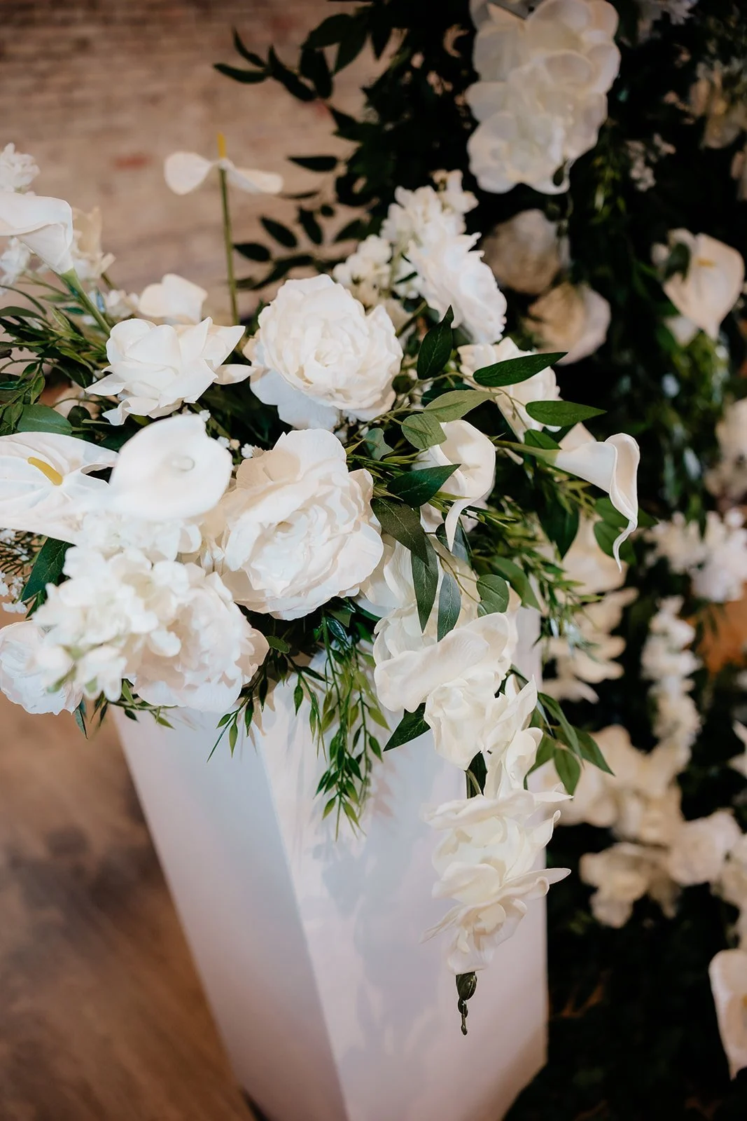 White floral arrangement with peonies, calla lilies, and greenery in a white rectangular vase.