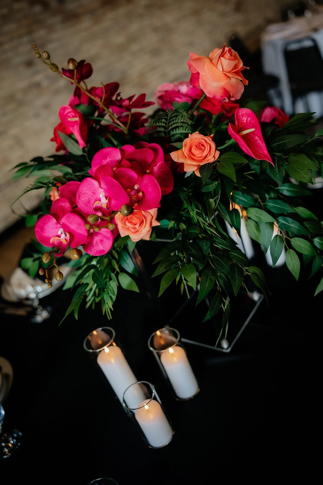 A floral arrangement with pink orchids, orange roses, and greenery, illuminated by small candles placed nearby.