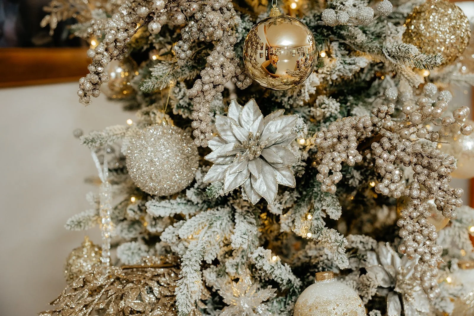 Decorated Christmas tree with white, gold, and silver ornaments including a large gold bauble, a glittery sphere, a silver poinsettia, and gold bead garland.
