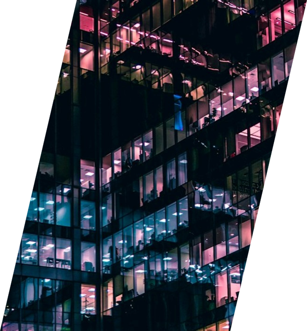 Nighttime view of a glass office building with illuminated interior rooms in pink, blue, and purple lights.