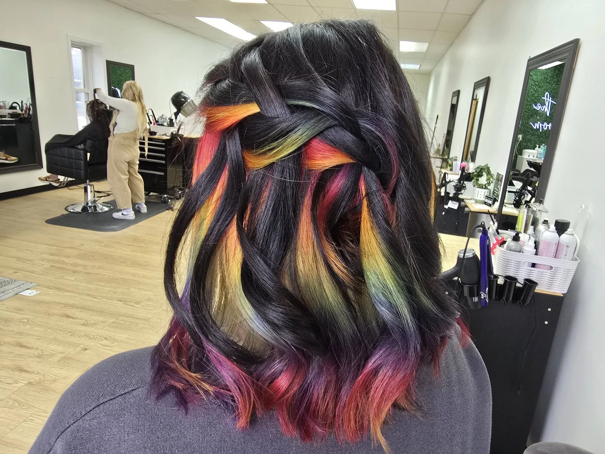 Close-up of a woman's hair styled in a braid with colorful dye on the ends in a salon.