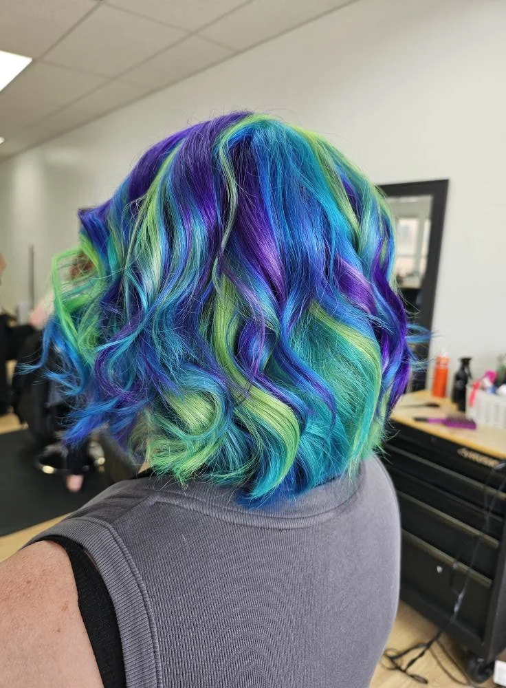 Colorful rainbow hair with blue, purple, green, and yellow curls in a salon setting.