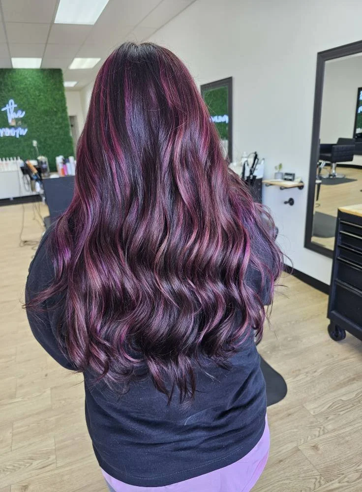 Back view of a woman with long, wavy hair in shades of purple and pink in a hair salon.