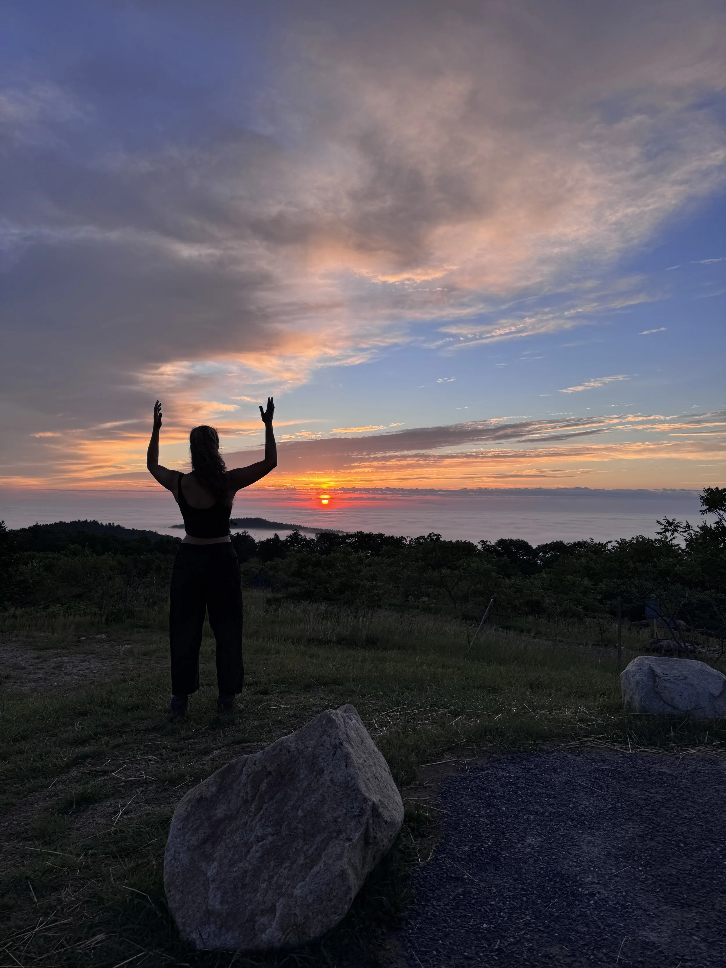 Erika practicing Qigong outdoors at sunset with arms raised toward the sky.