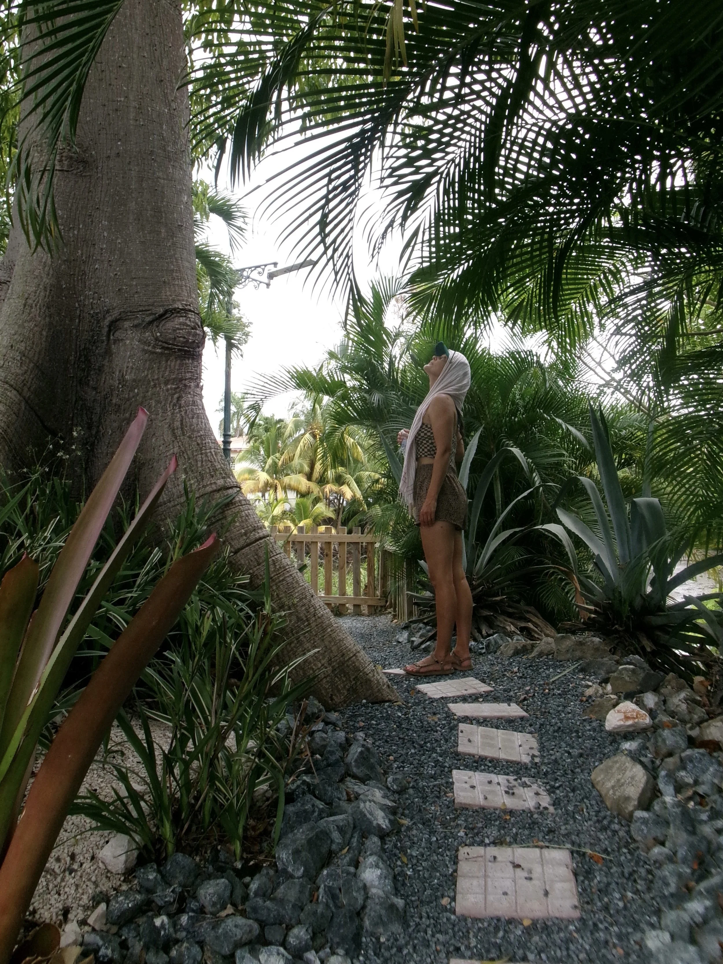 Erika standing on a peaceful garden path surrounded by lush greenery.
