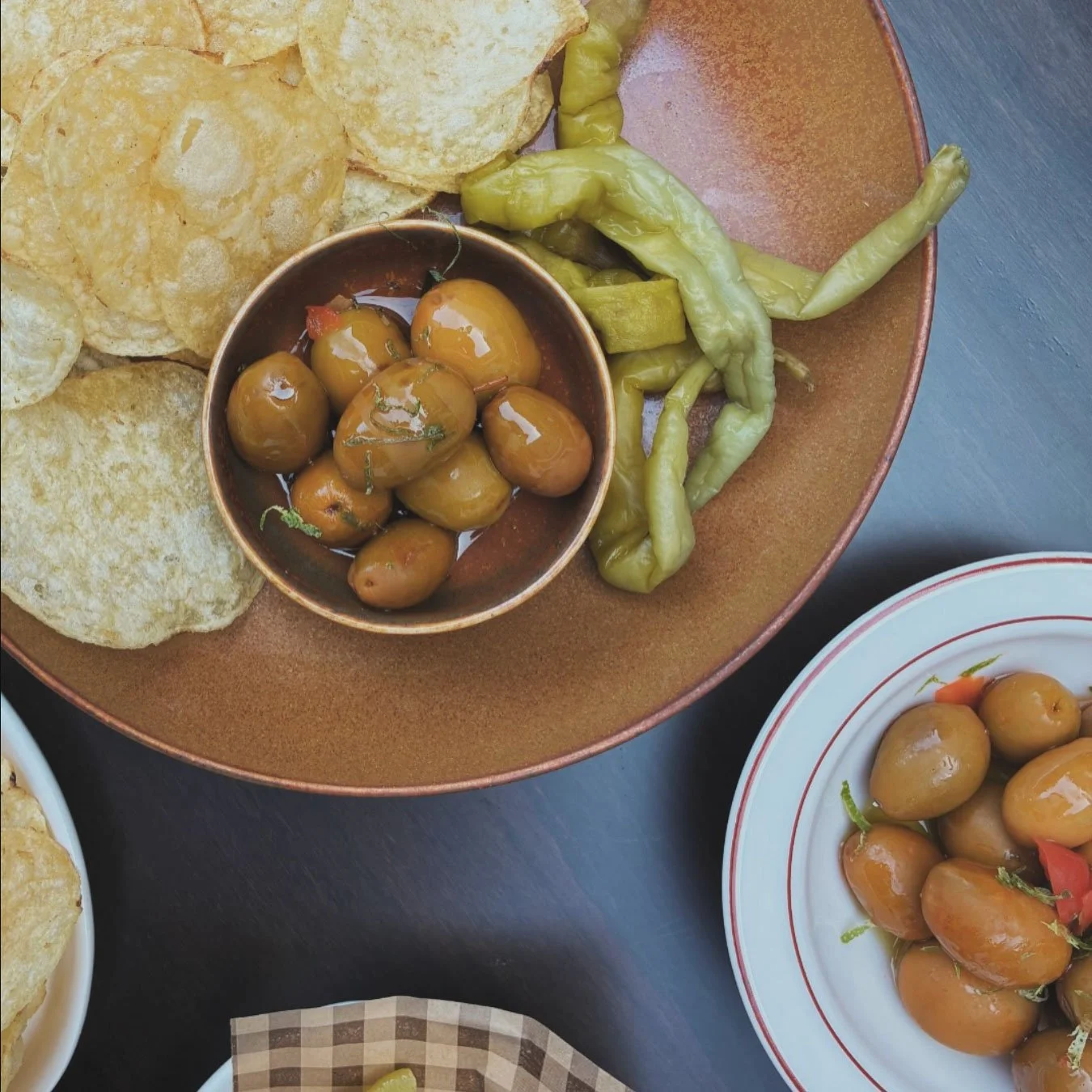 Plate with blistered sishito peppers, crisps, and a small bowl of green olives