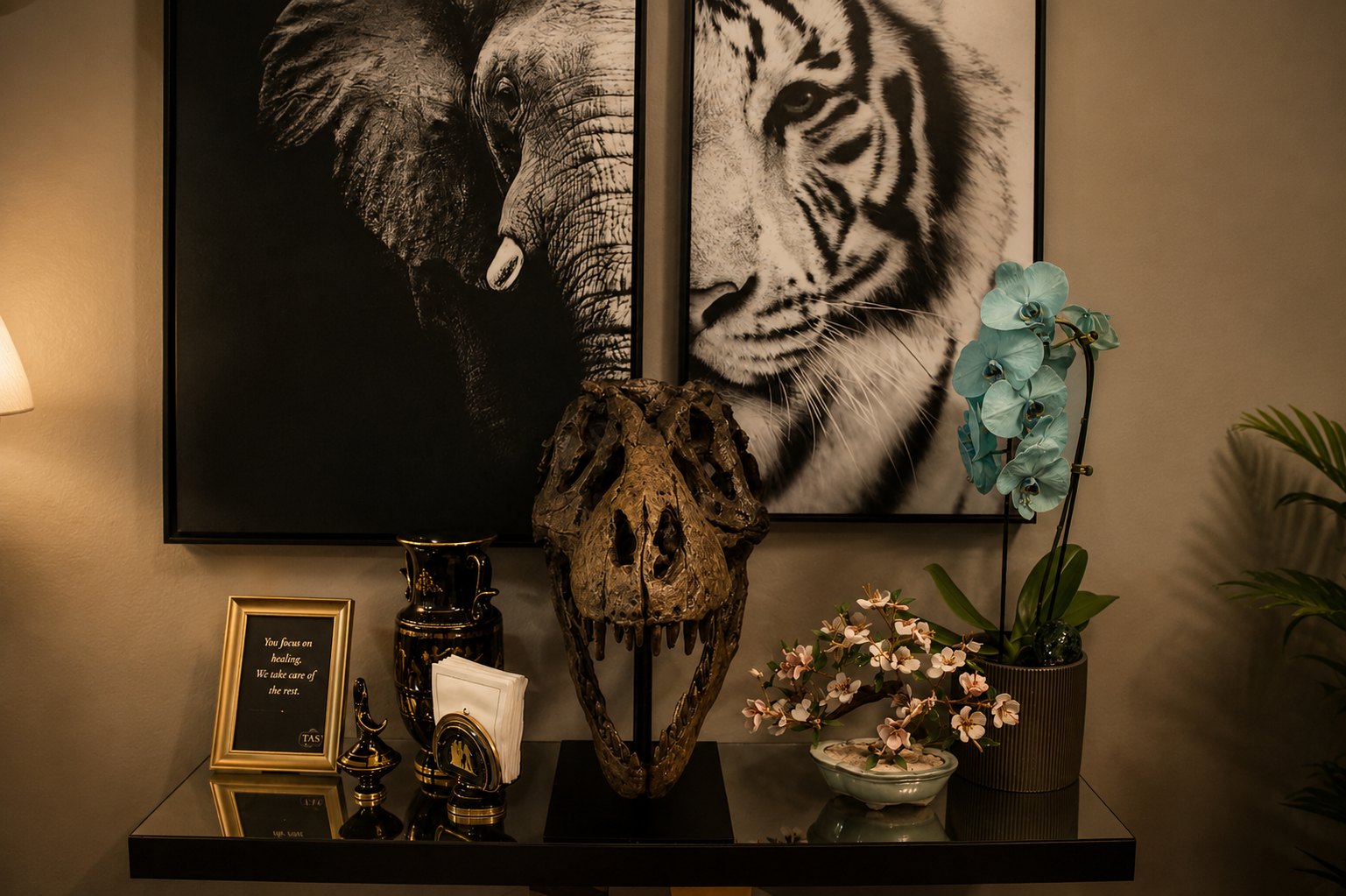Decorative display with animal-themed artwork, a skull sculpture, orchids, and framed quote on a black table.