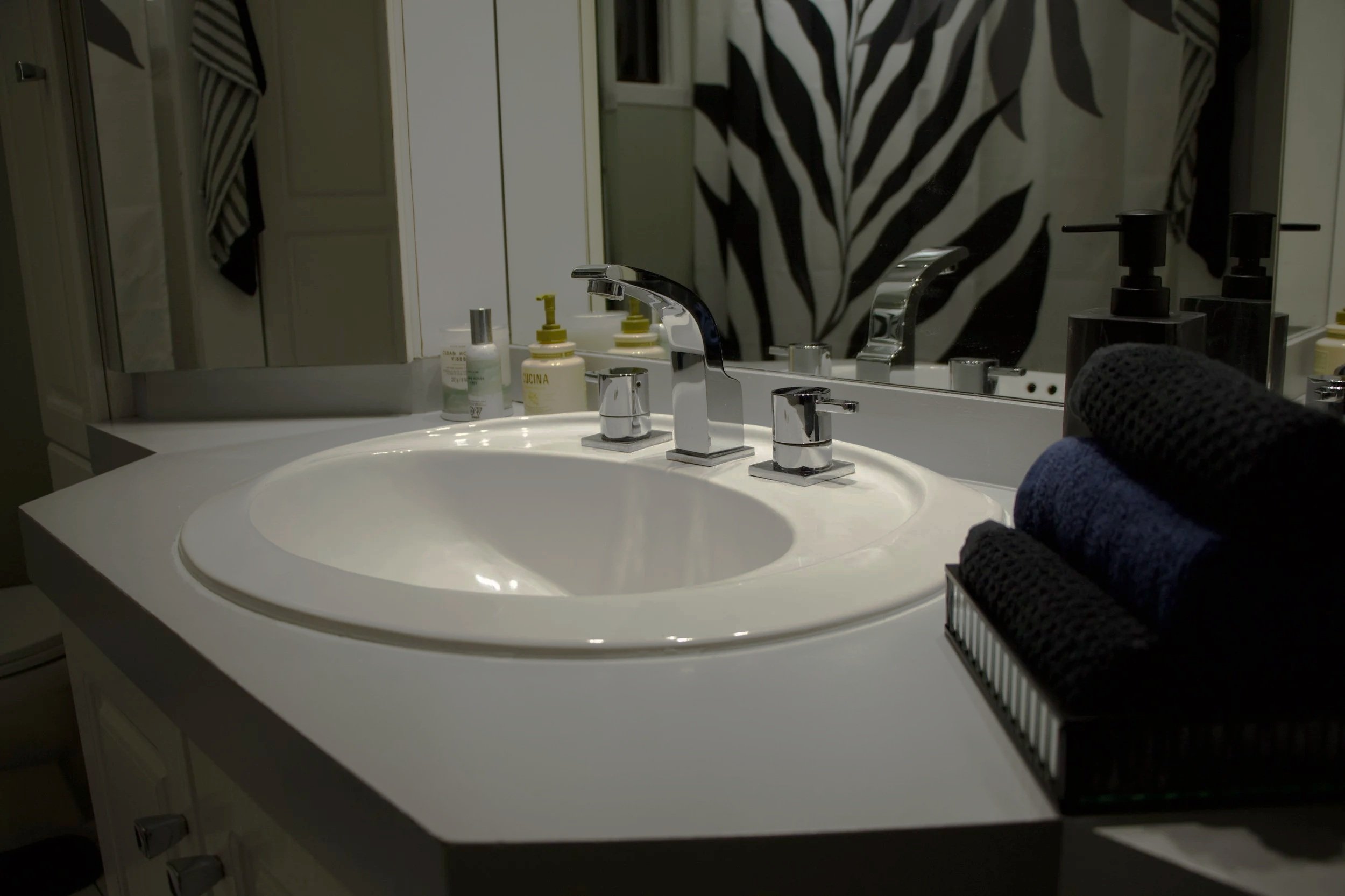 Bathroom sink with a mirror, soap dispensers, and hand sanitizer on the countertop. Towels are hanging on the wall, and a decorative zebra-striped shower curtain is visible in the background.