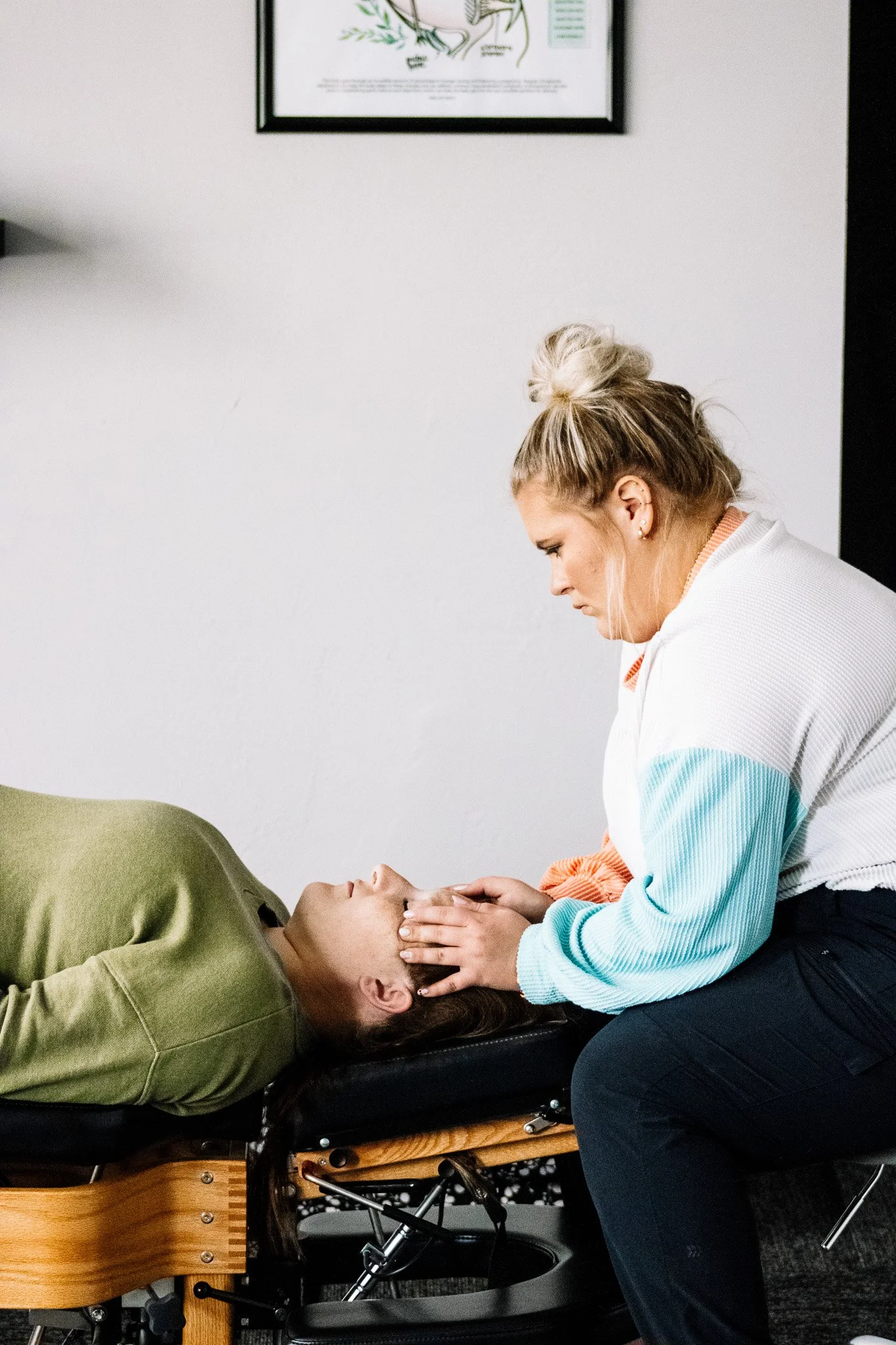 A woman lying in a wheelchair with her eyes closed, being attended to by another woman who is gently holding her face and looking at her.