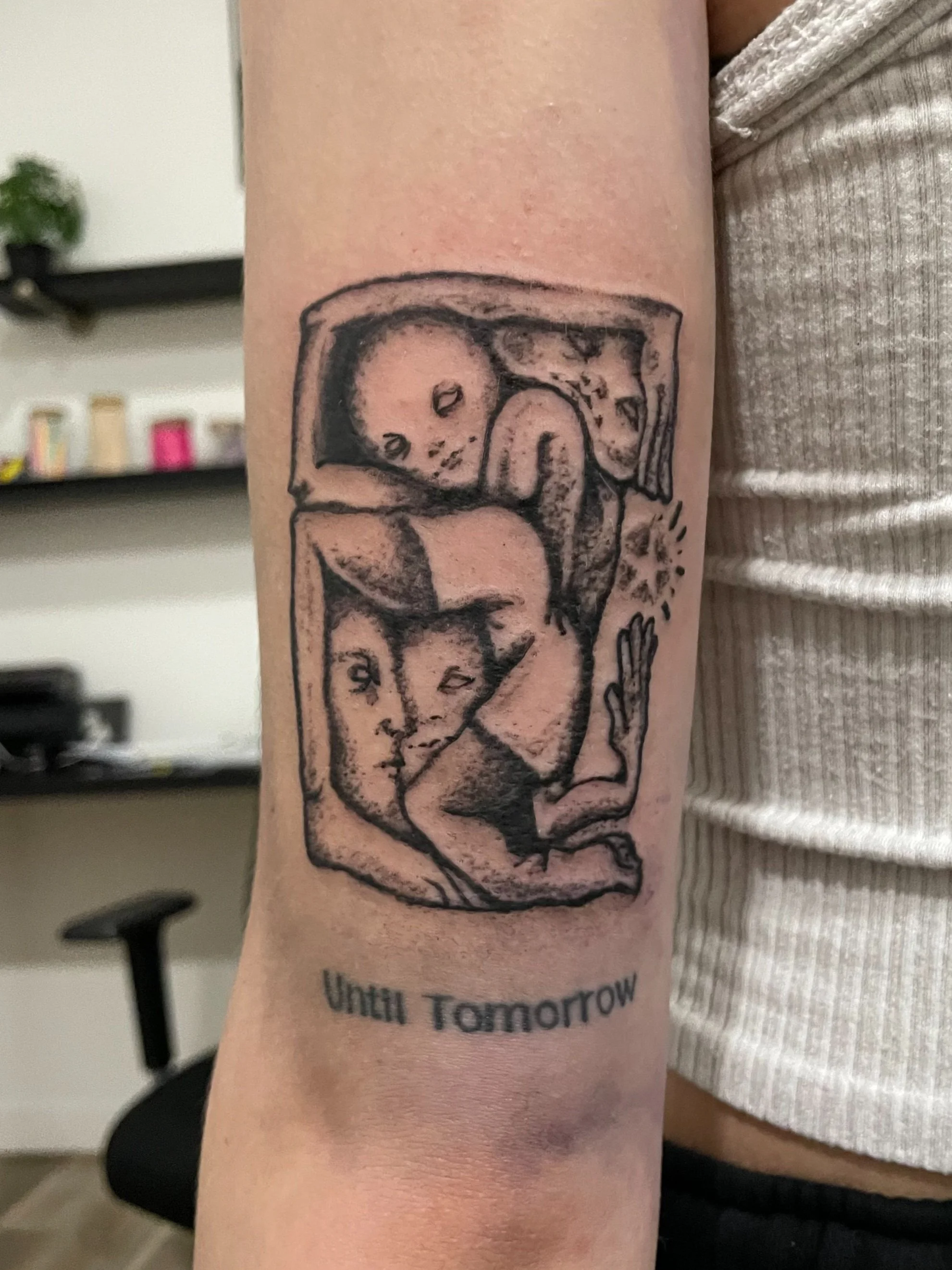 Tattoo of an abstract, sketch-like illustration of a face with a hand, enclosed in a rectangular frame, with the words "Until Tomorrow" underneath.