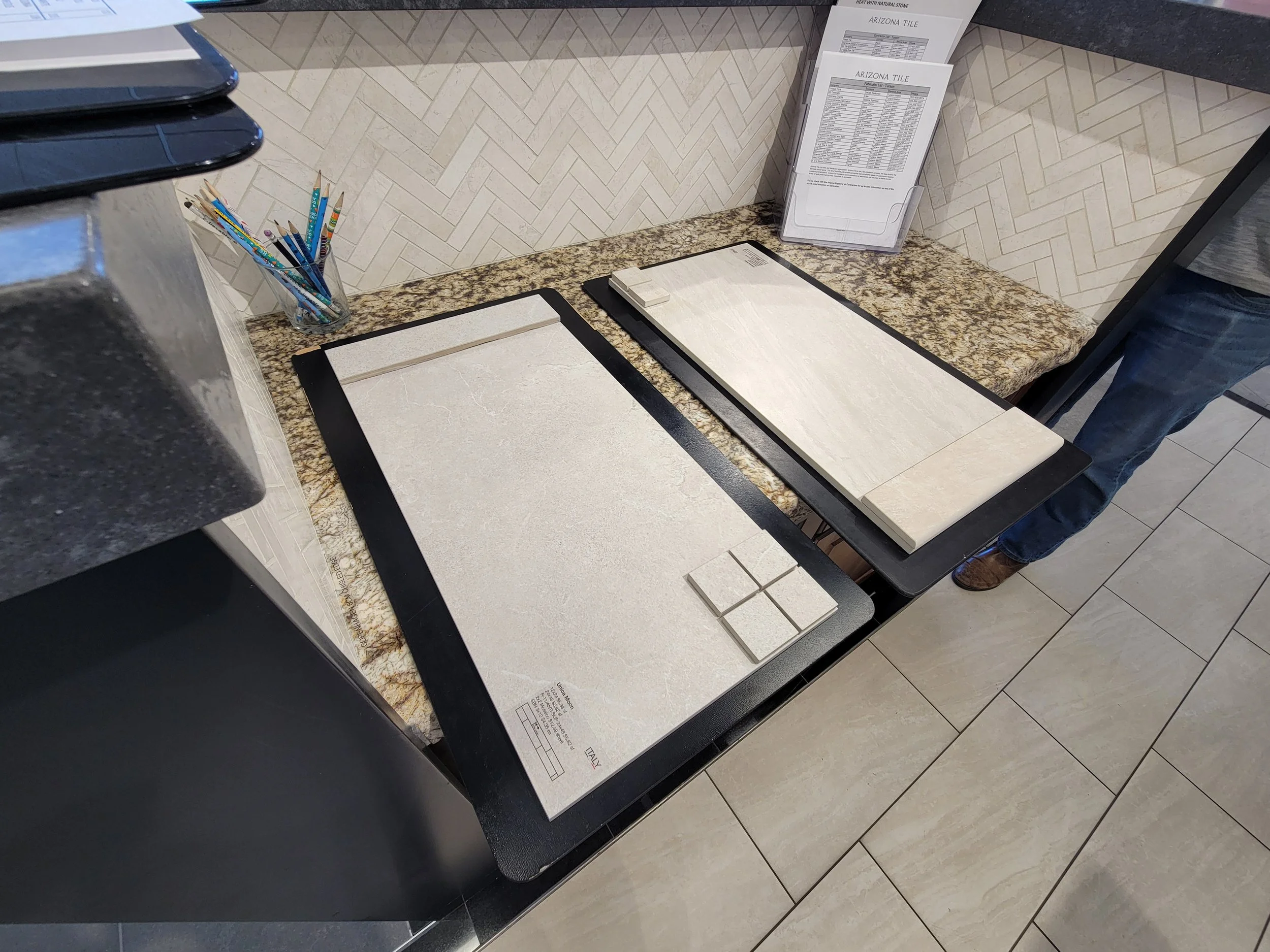 Samples of tile displays on a granite countertop at a showroom, with a container of colored pencils and informational pamphlets in the background.
