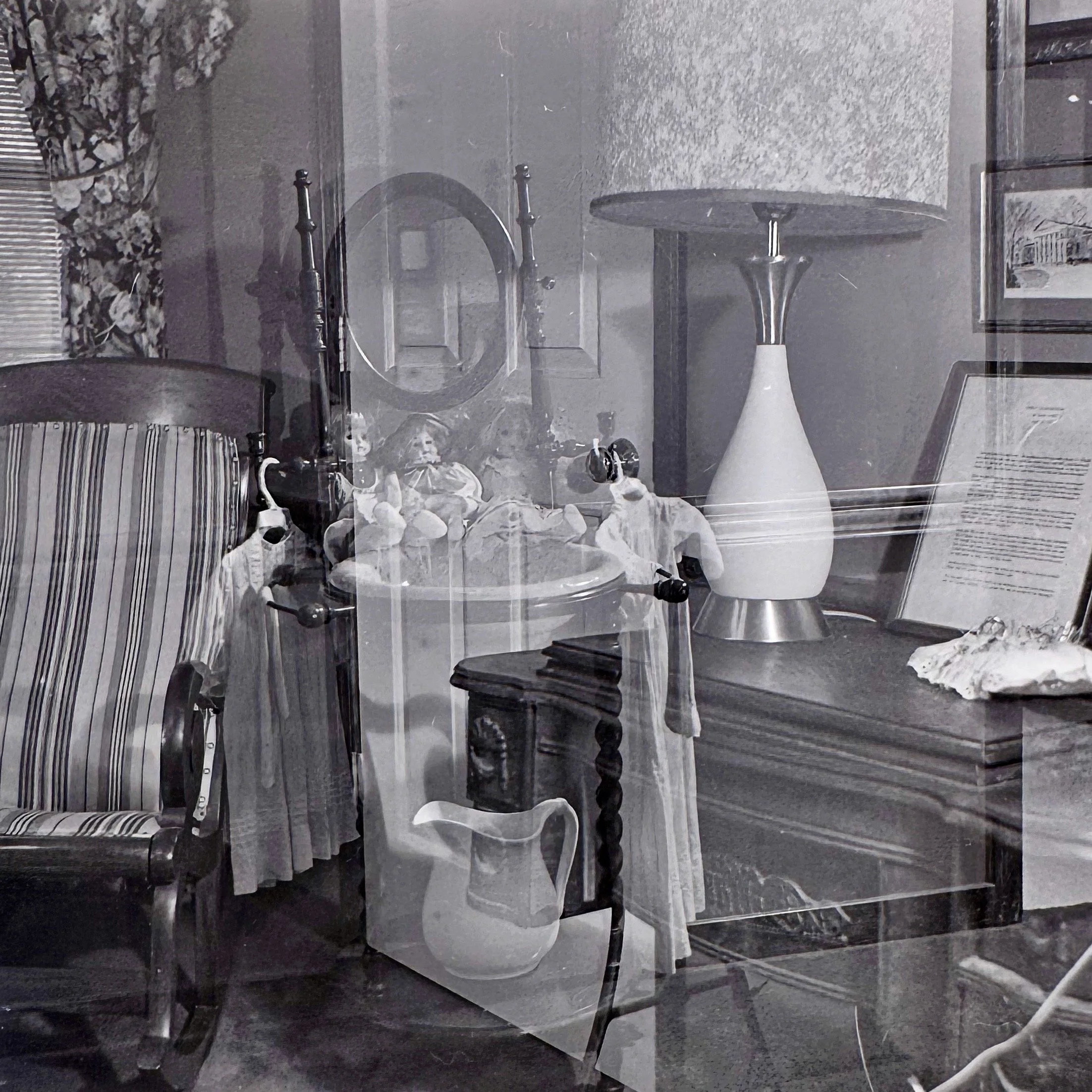 Reflection of a dining room with a round table, decorative vases, framed picture on the wall, and a patterned curtain.