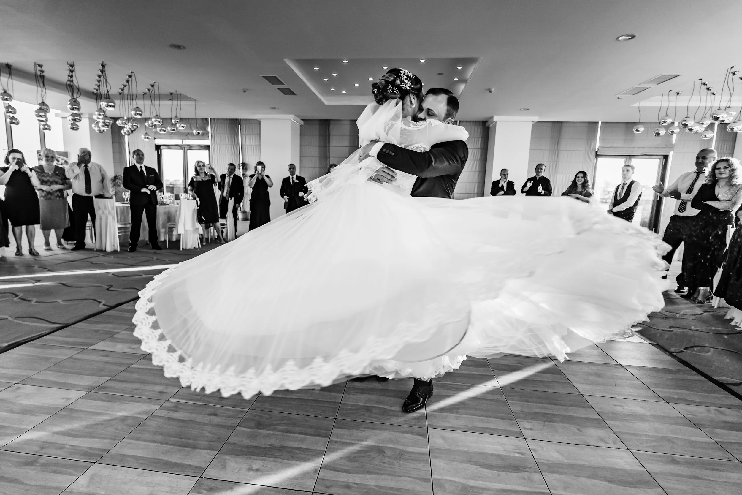 A bride and groom sharing a dance at their wedding reception, surrounded by guests in a modern decorated venue.