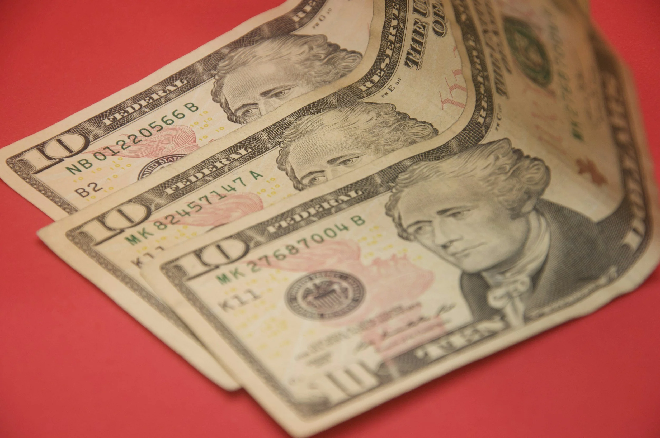 Three ten-dollar bills spread out on a red surface.