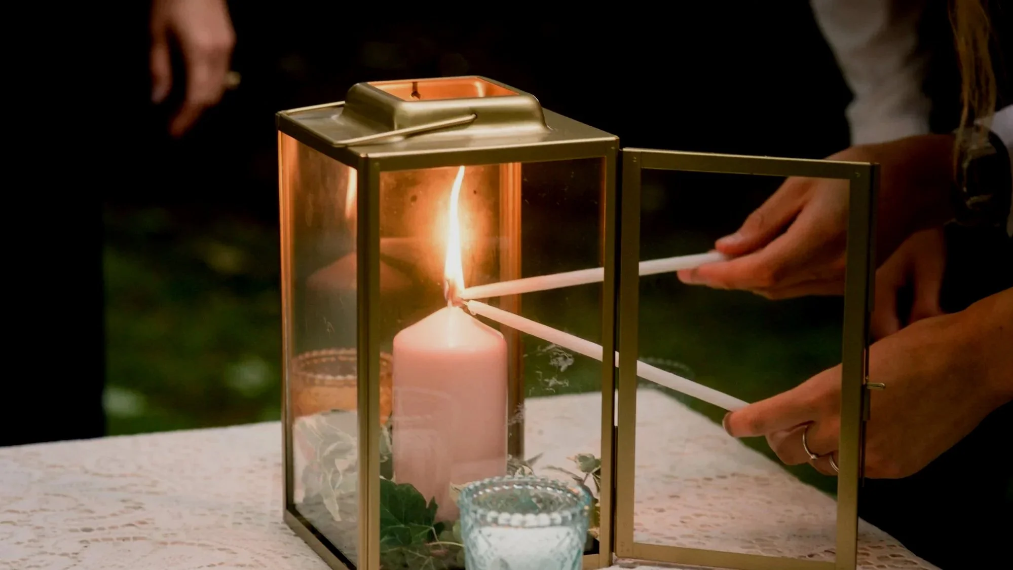 People relighting a candle inside a glass lantern at night.