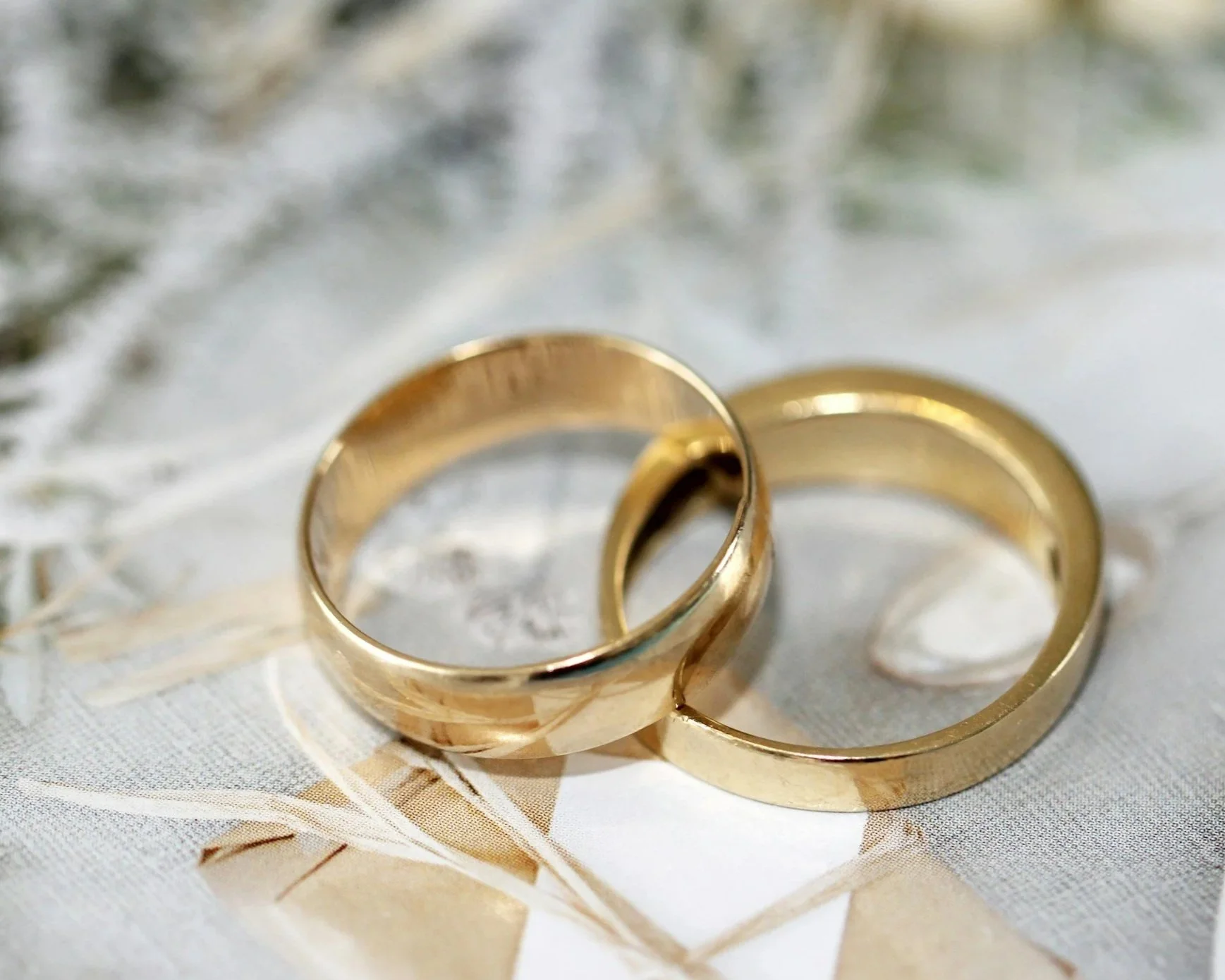 Two gold wedding rings on a fabric surface with a leaf pattern.