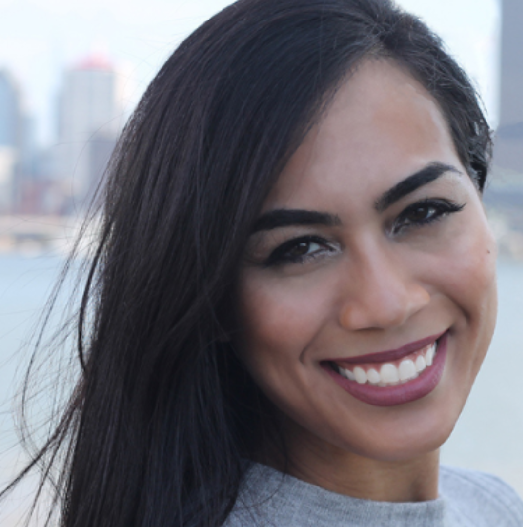 Close-up of a smiling woman with dark hair against a cityscape background.