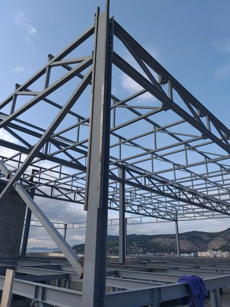 Estructura metálica en construcción en una azotea, con montañas y ciudad en el fondo, y cielo despejado.